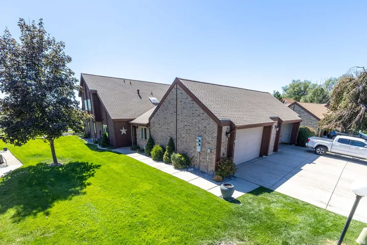 Brick and wood-finish exterior featuring a multi-car driveway, two garage doors, and a manicured lawn