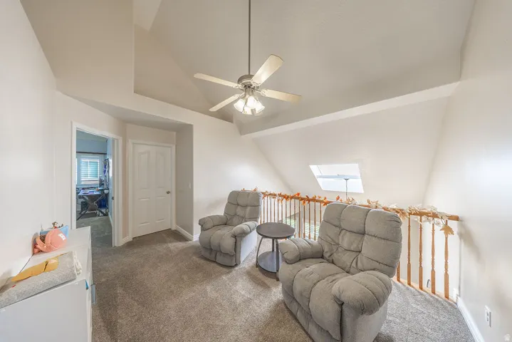 Carpeted loft space featuring an angled ceiling, ceiling fan with light fixture, and a skylight