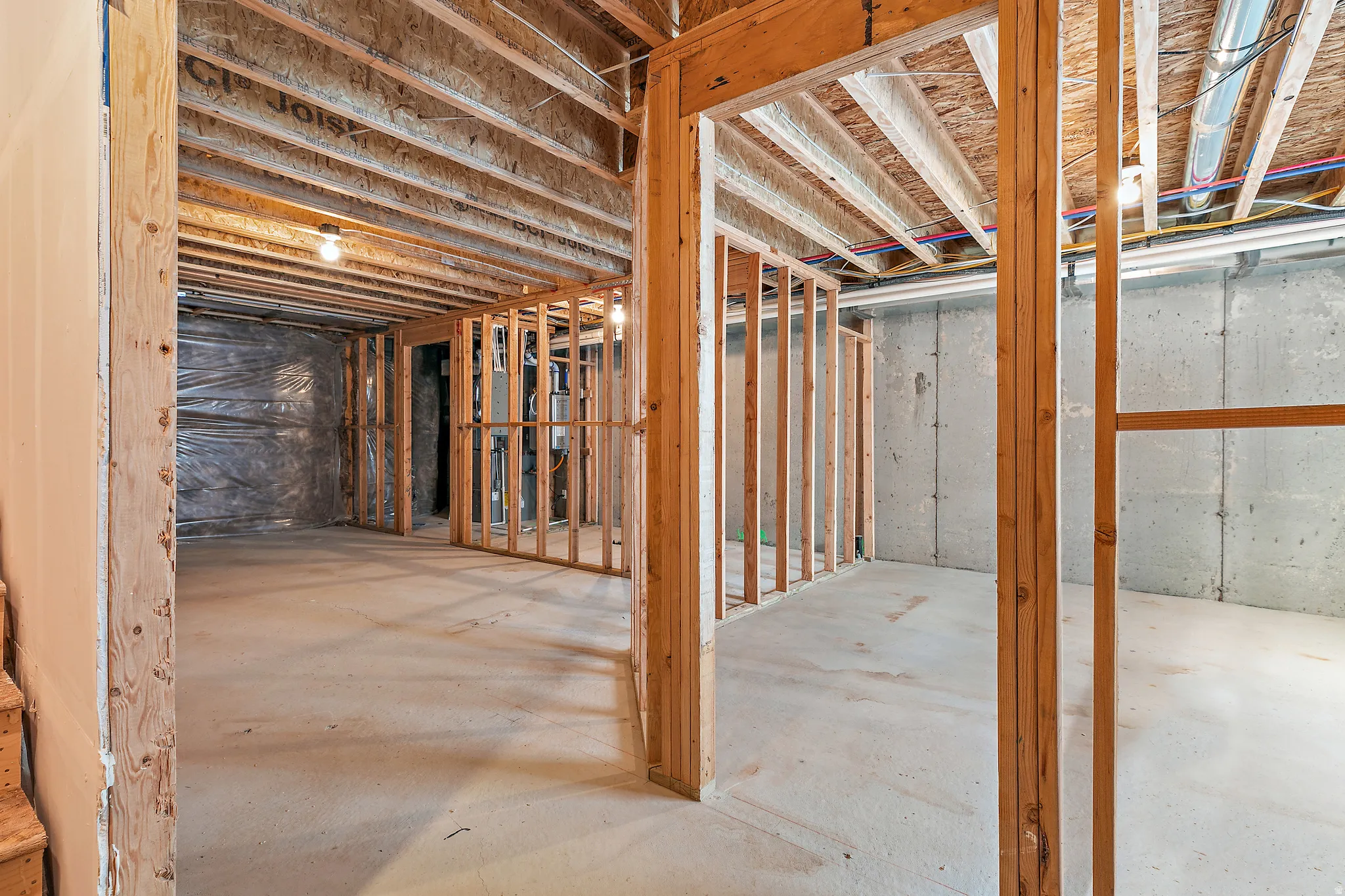 Unfinished basement featuring exposed wood joists and concrete walls