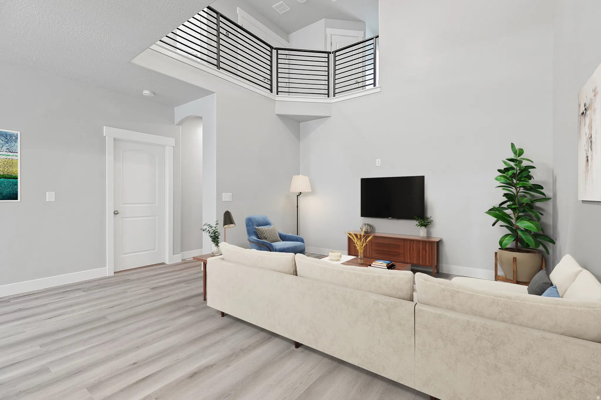 Open-concept living space featuring high ceilings, wood-finish flooring, a contemporary black metal railing, and light gray wall tones