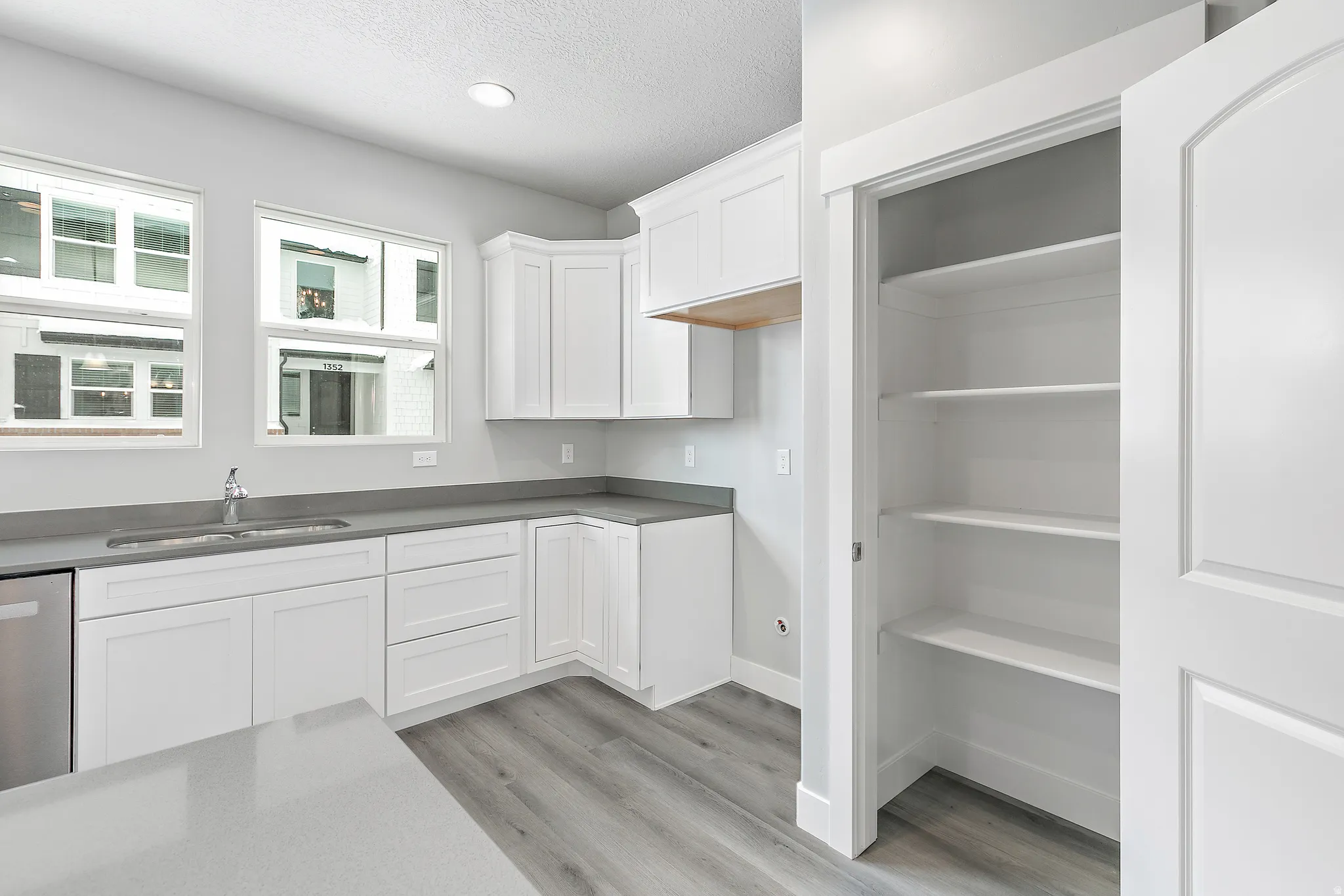 White cabinetry, gray countertops, recessed lighting, wood-finish flooring, and a built-in pantry