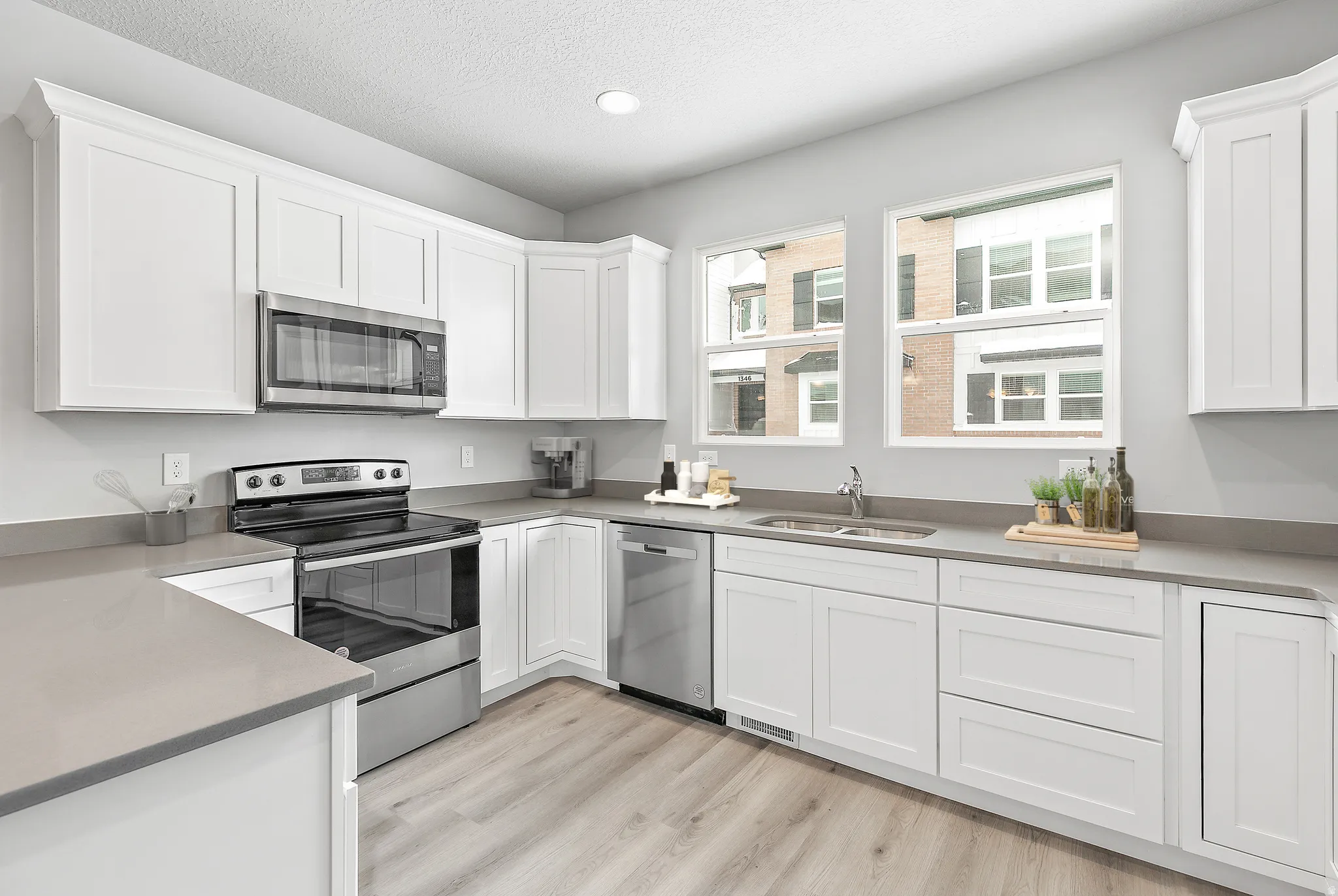 White shaker-style cabinetry, stainless steel appliances, light gray countertops, recessed lighting, and wood-finish flooring