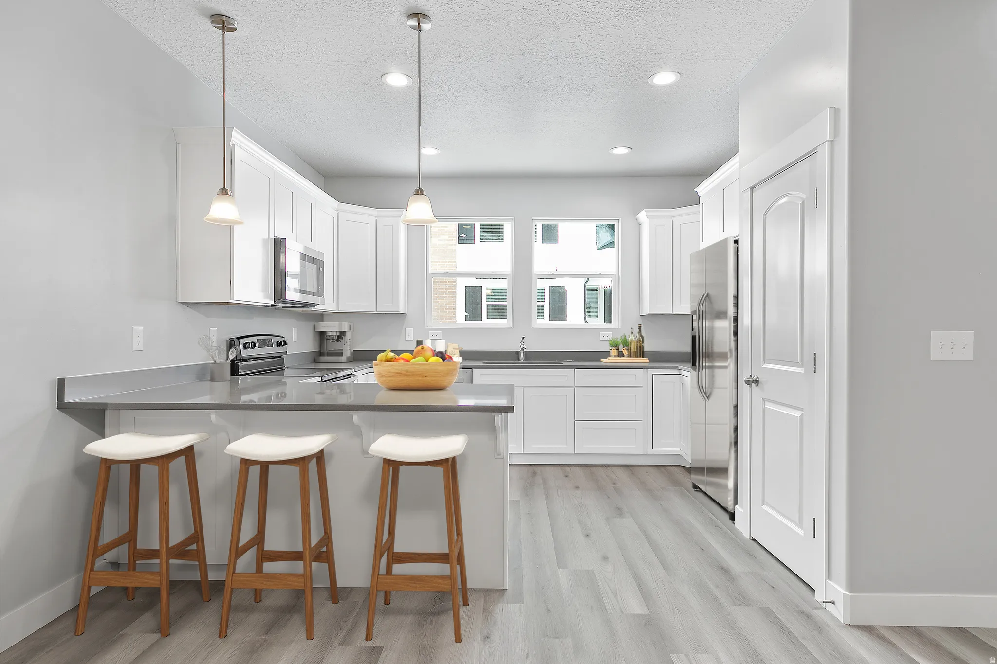 Modern kitchen featuring white cabinetry, stainless steel appliances, a breakfast bar with an overhanging countertop, and wood-finish flooring