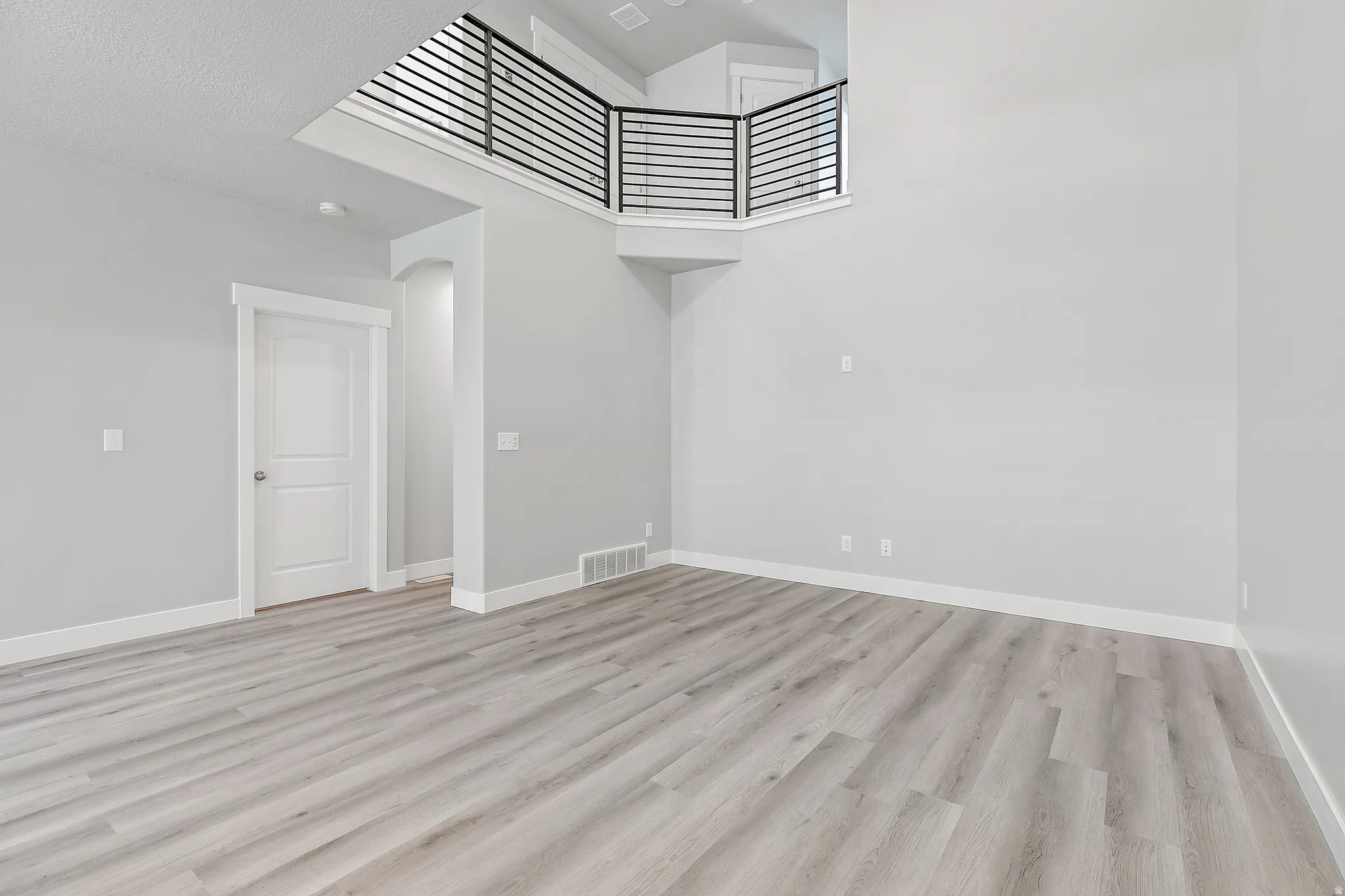 Spacious room featuring wood-finish flooring, light gray wall paint, and a second-story landing with horizontal metal railings