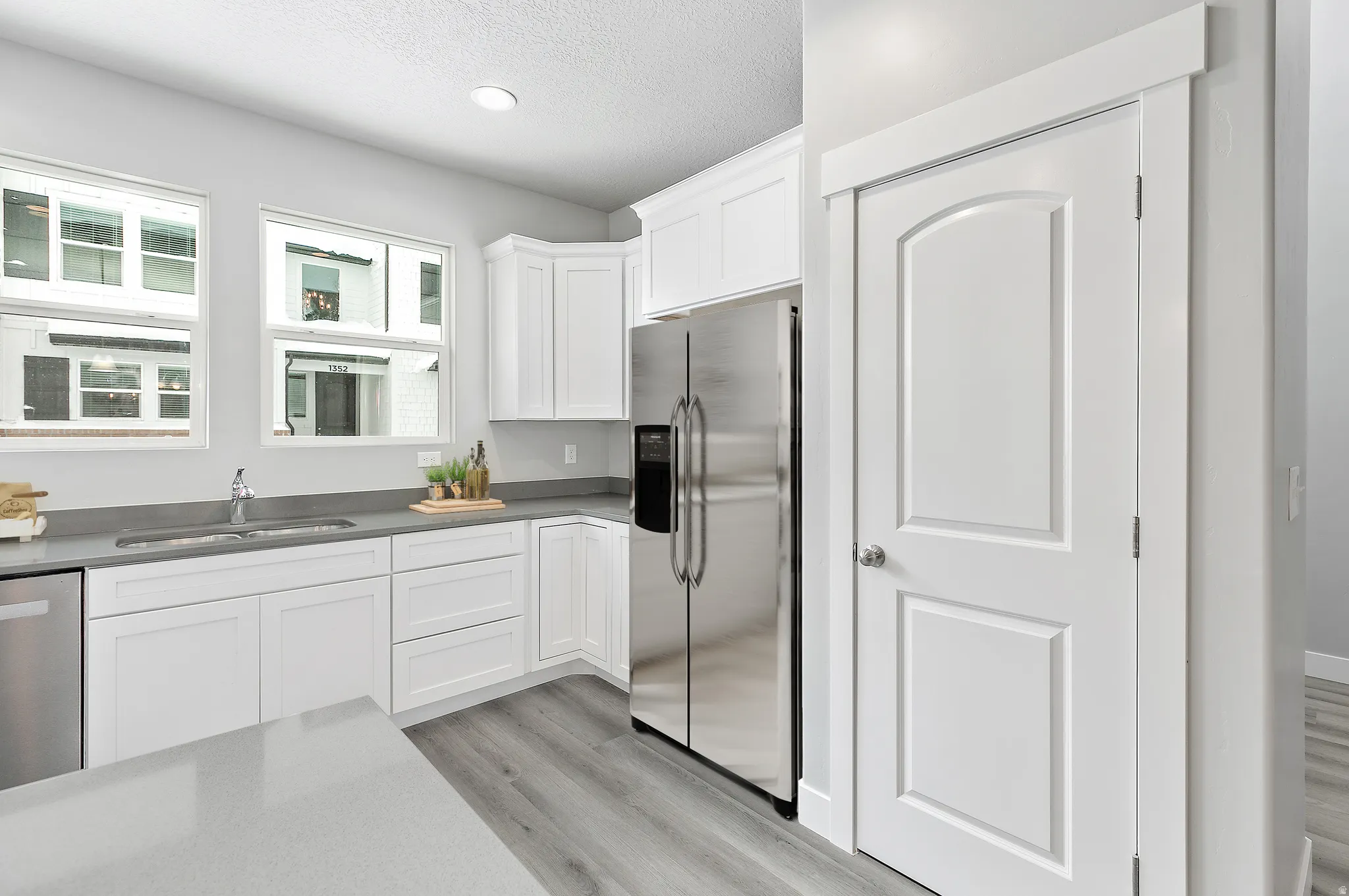 White cabinetry, stainless steel appliances, grey countertops, wood-finish flooring, and recessed lighting