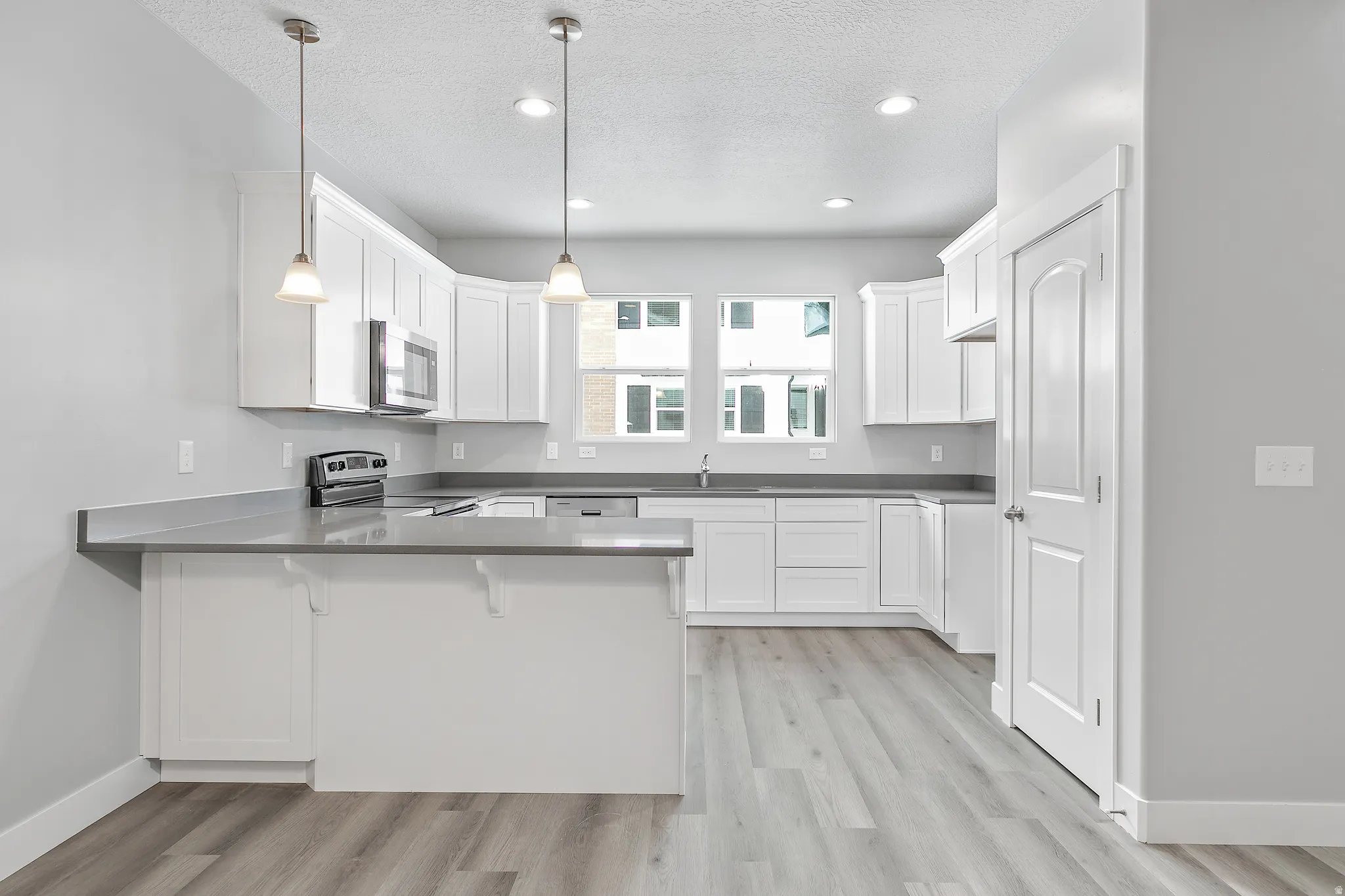 Modern kitchen featuring white cabinetry, grey countertops, stainless steel appliances, a center island, and wood-finish flooring