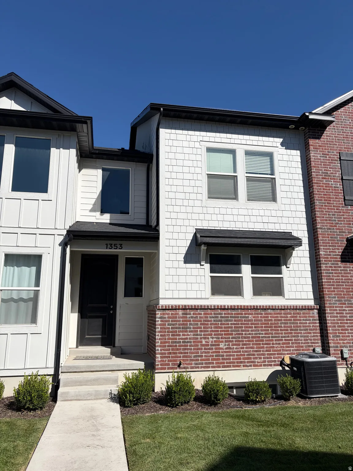 White vertical siding with shake accent panels, brick detailing, black trim, and a prominent dark entry door