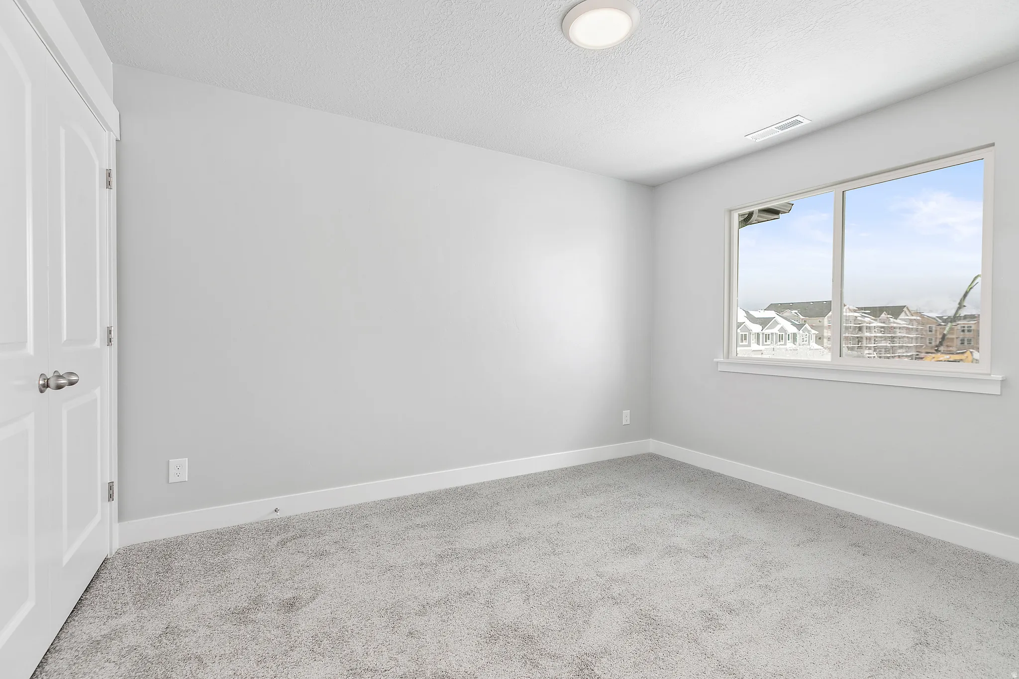 Neutral gray walls, plush gray carpeting, white trim, recessed ceiling light, and a large window