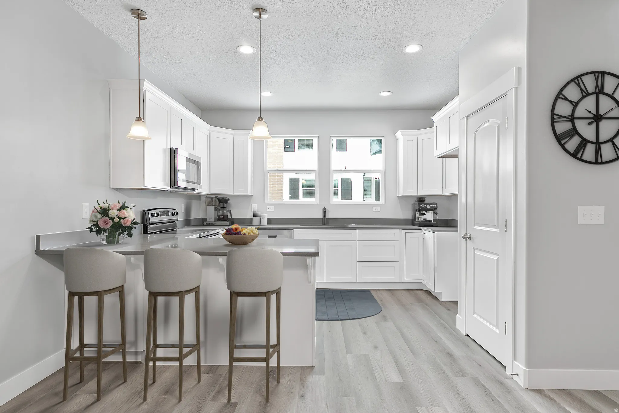 Contemporary kitchen featuring white cabinetry, gray countertops, stainless steel appliances, pendant lighting, and wood-finish flooring