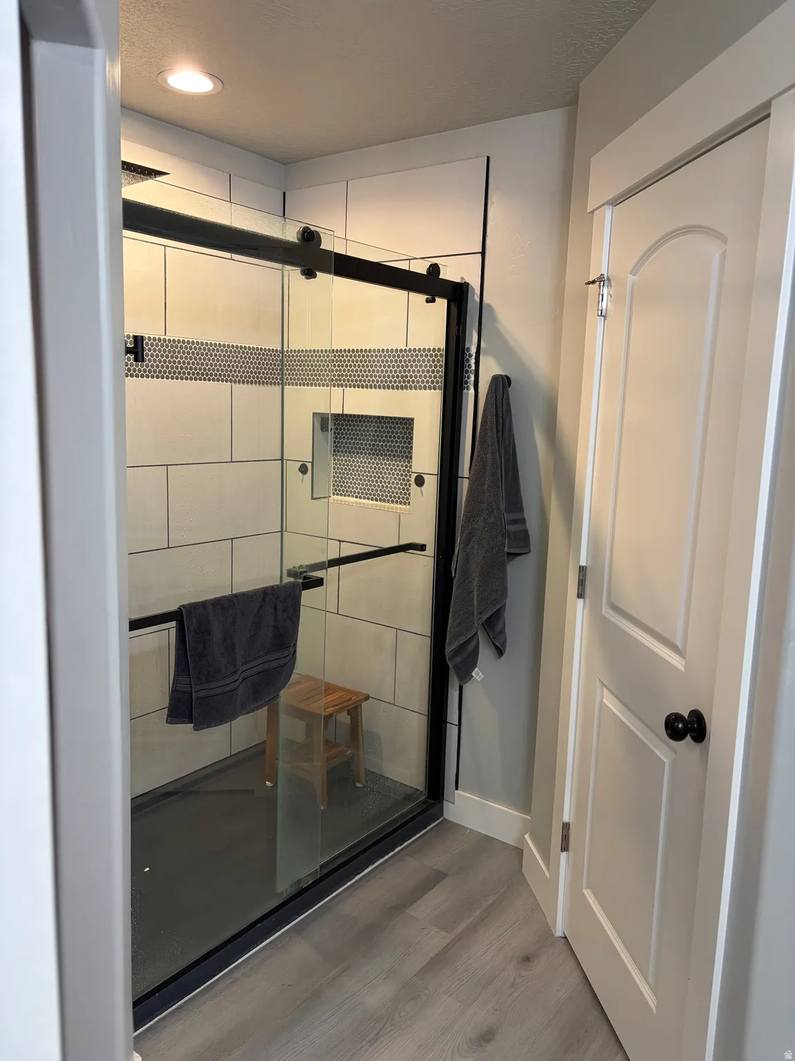 Walk-in shower with clear glass enclosure and black hardware, featuring a tiled accent band and built-in niche