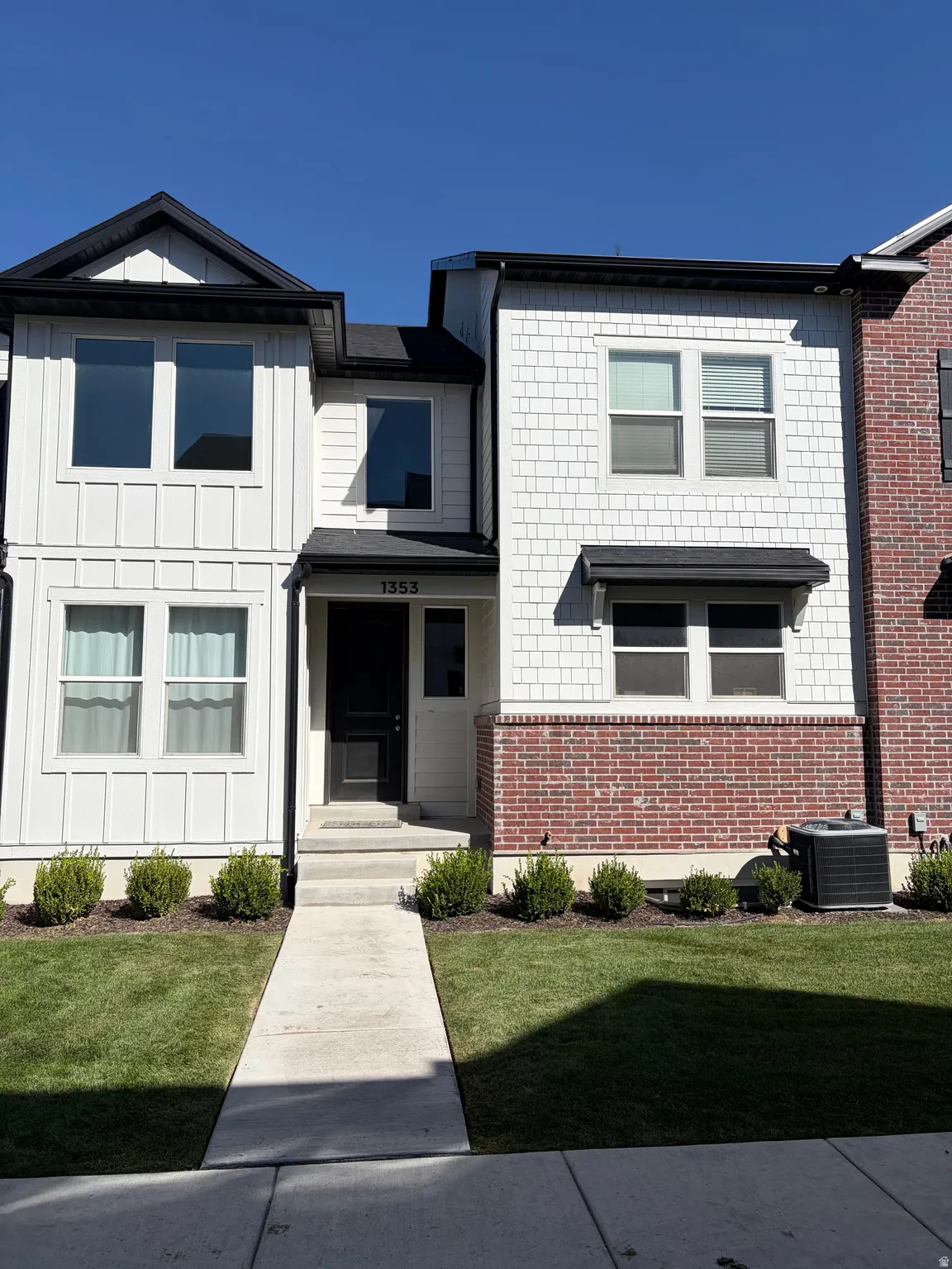 Modern exterior featuring white vertical board and batten siding, white shake siding, red brick accents, and a black front door