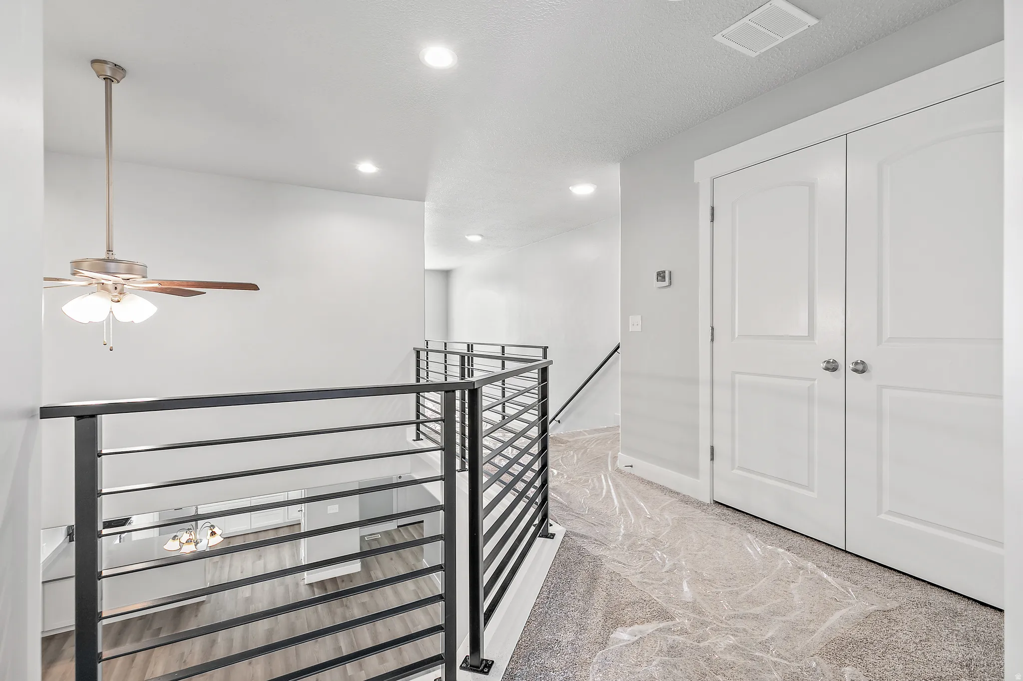 Open-concept interior featuring a black metal horizontal bar railing, recessed ceiling lighting, and a ceiling fan with light
