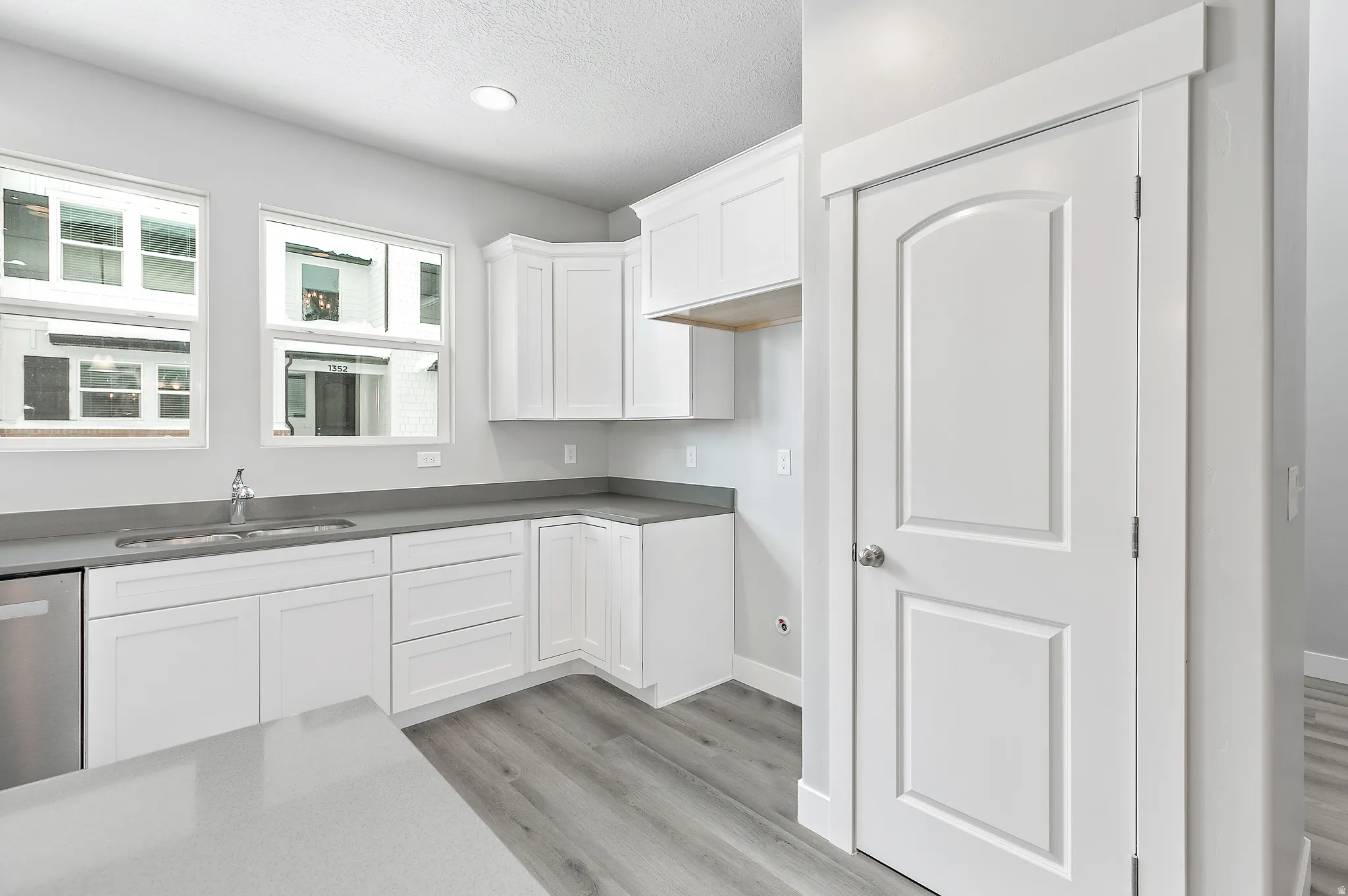 White cabinetry with chrome hardware, grey countertops, stainless steel dishwasher, and wood-finish flooring