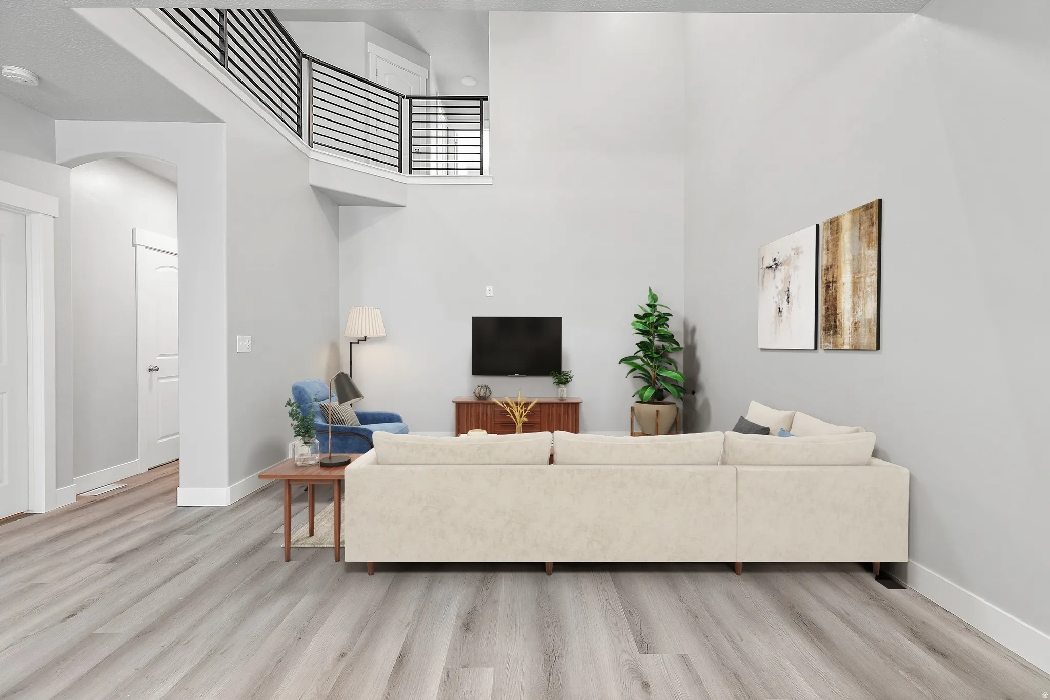 Light gray walls, wood-finish flooring, vaulted ceiling, and an upper-level balcony with black metal railings