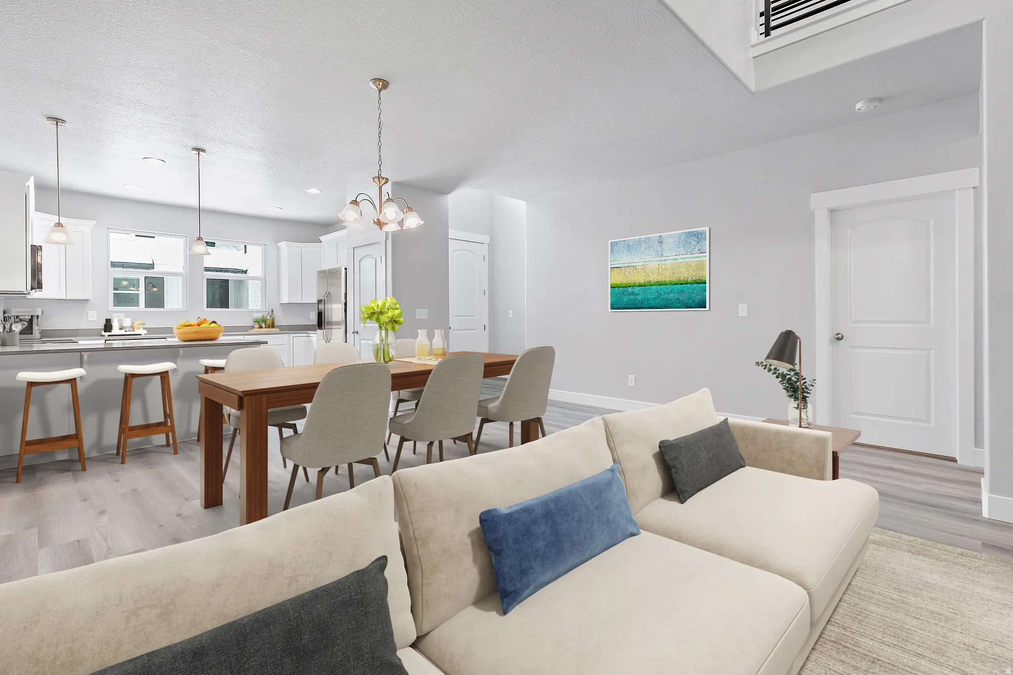 Open-concept living area featuring light wood-finish flooring, white walls, and a modern kitchen with a breakfast bar