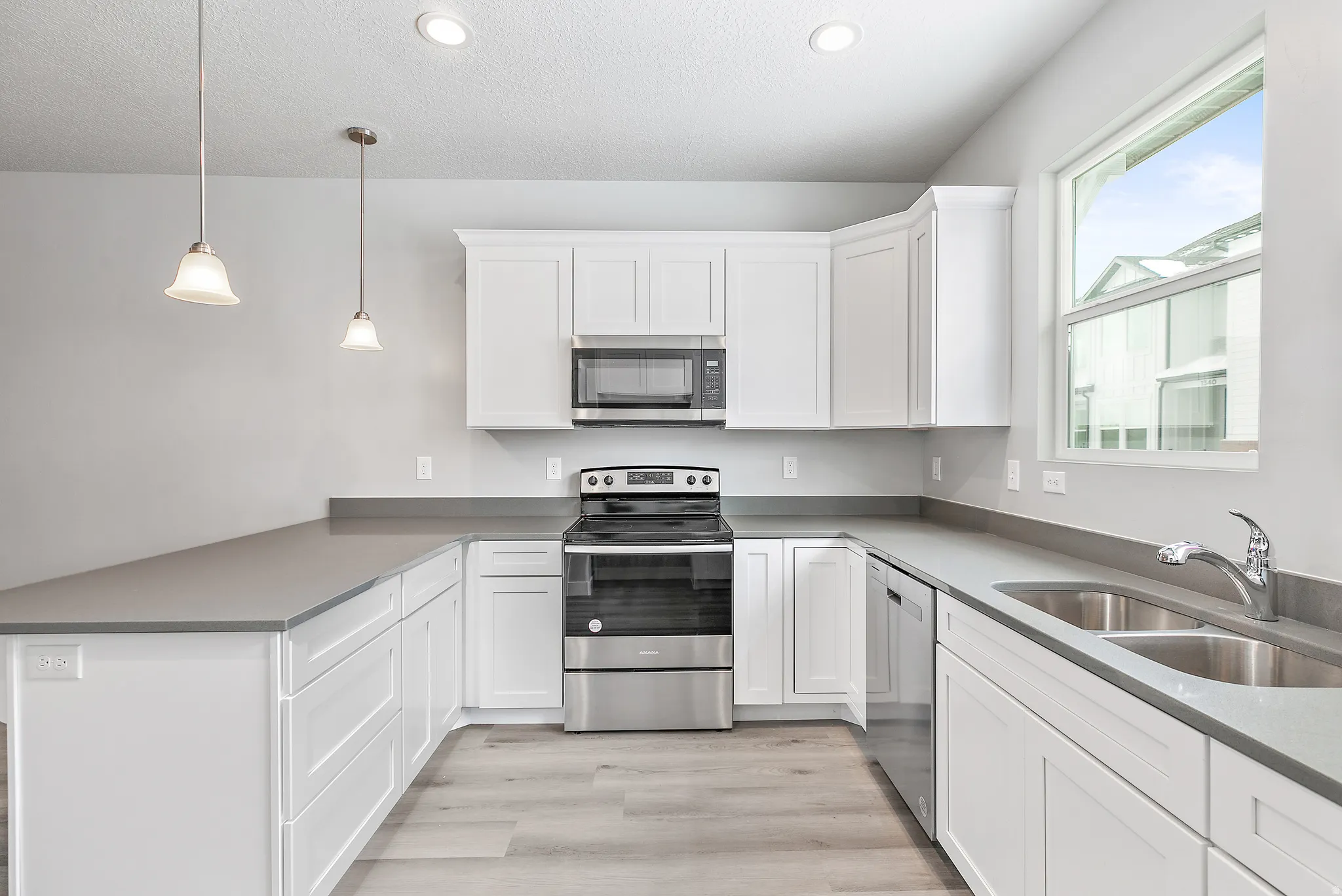 Modern kitchen featuring white cabinetry, grey countertops, stainless steel appliances, wood-finish flooring, and pendant lighting