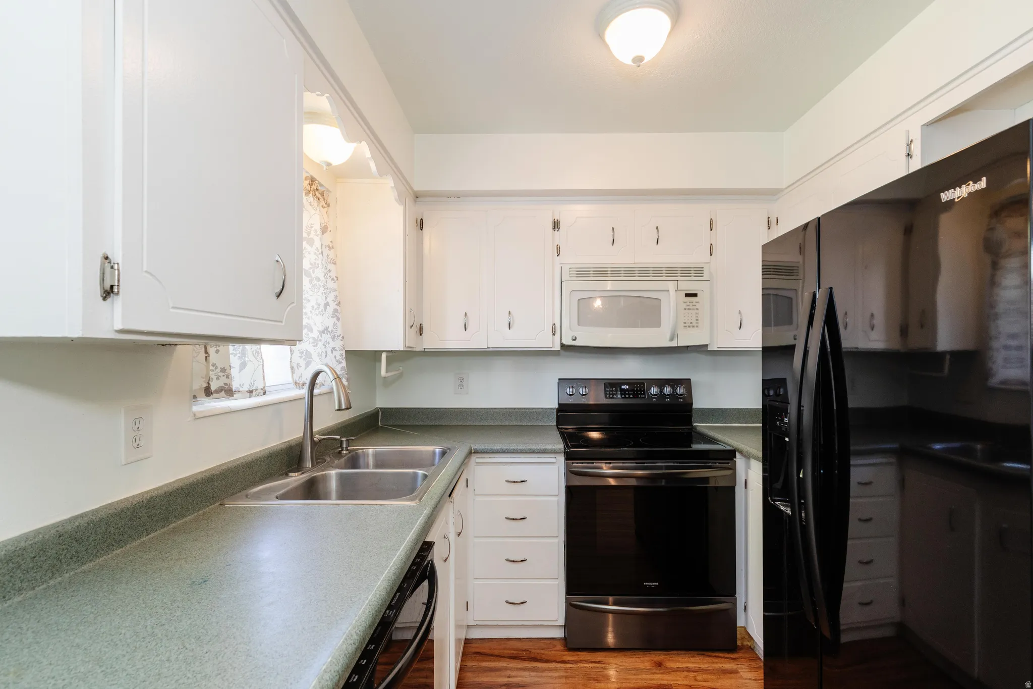 White cabinetry, dual basin stainless steel sink, integrated microwave, black electric range, and wood-finish flooring