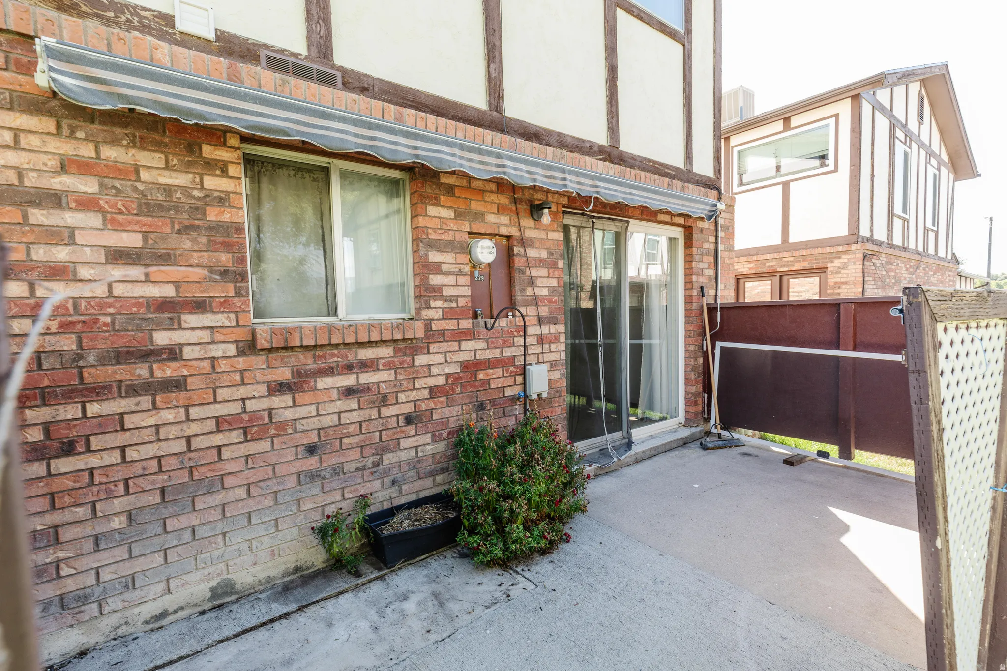 Brick exterior, sliding glass door, concrete patio, privacy screen, overhead awning