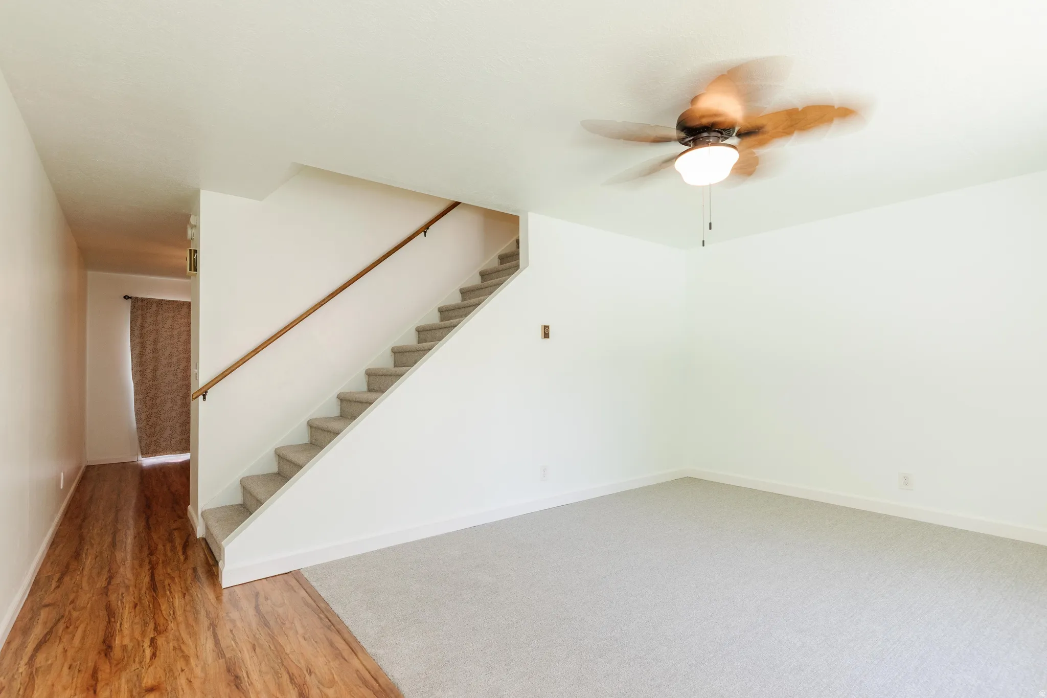Living area featuring a ceiling fan, light gray carpet, and wood-finish flooring