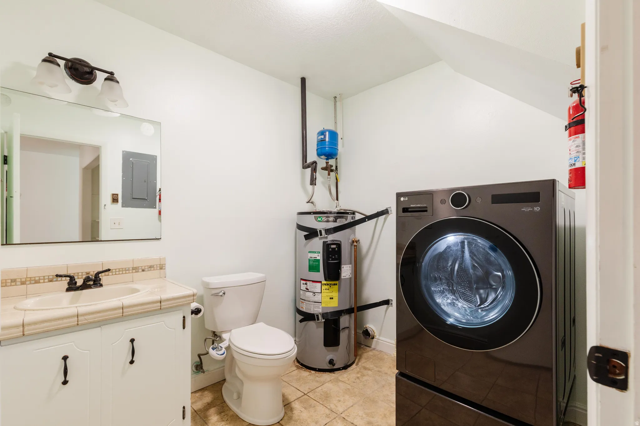 Vanity with an integrated sink and tiled countertop, a full-sized toilet, and a washer