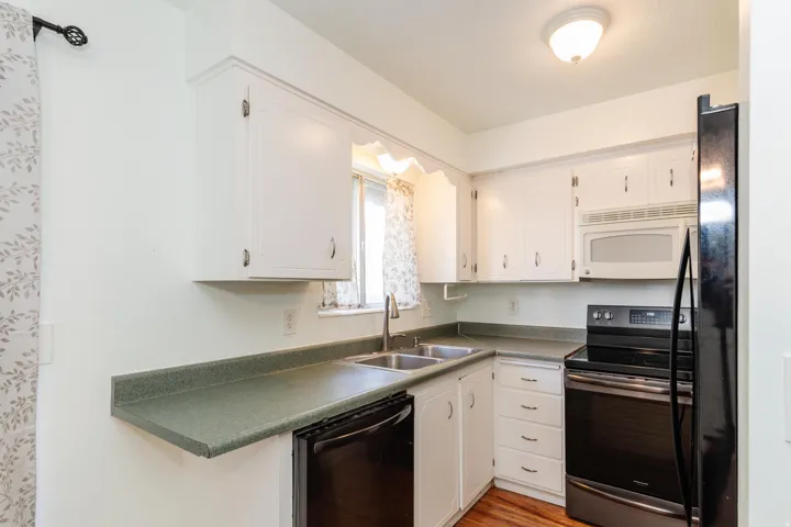 Kitchen featuring white cabinetry, a double basin sink, black range, black dishwasher, and white microwave