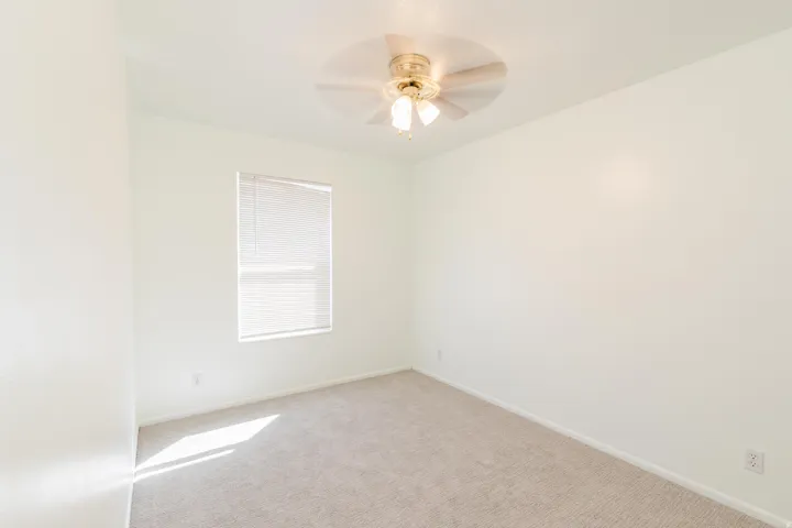 Recessed window with horizontal blinds, overhead ceiling fan with light fixture, light neutral wall paint, and plush carpet flooring