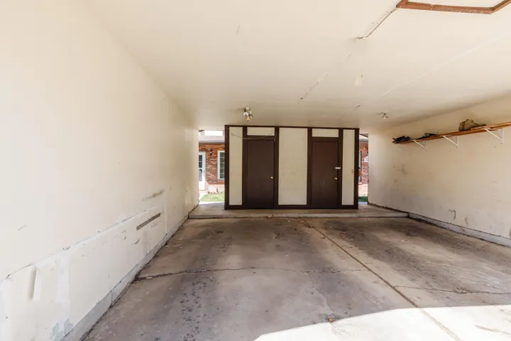 Covered carport with a concrete floor, two built-in storage doors, and overhead lighting