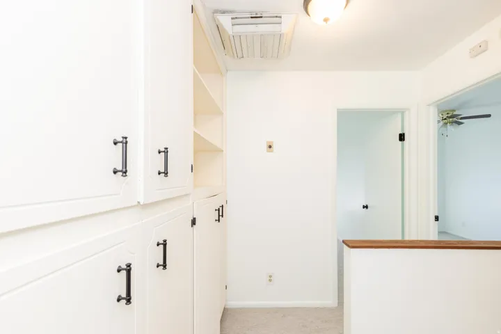 Built-in white cabinetry with dark pulls, integrated shelving, and carpet flooring