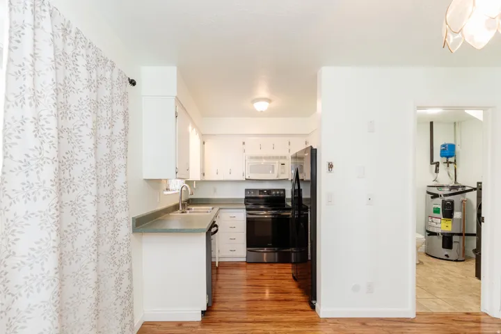 Kitchen featuring white cabinetry, dark countertops, wood-finish flooring, and a full suite of black and white appliances