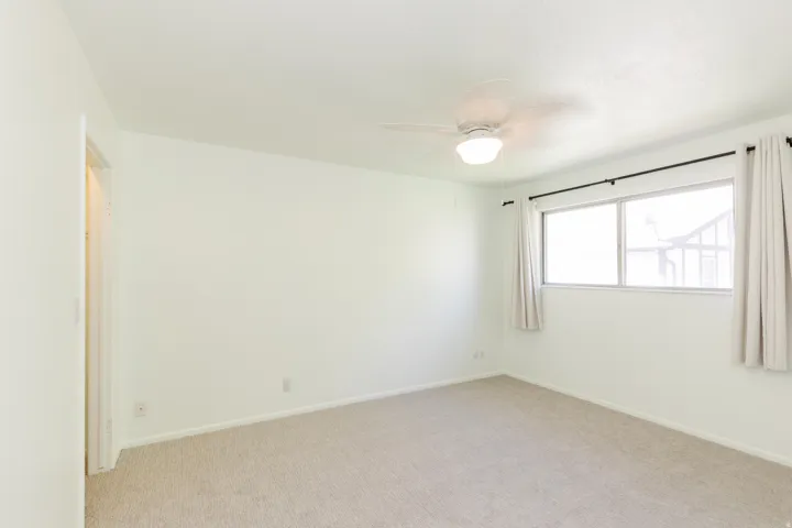 Wall-to-wall carpeting, overhead ceiling fan with light, and a window with curtain rods