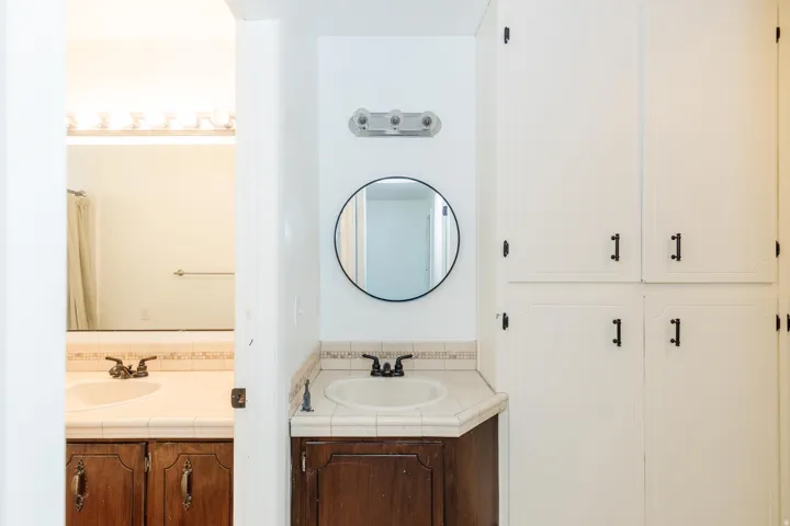 Dual vanity area featuring wood-finish cabinetry, tile countertops, and integrated sinks