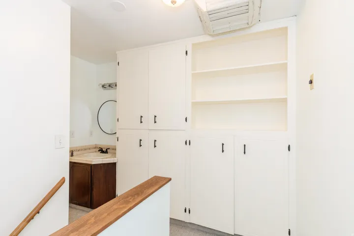 Built-in cabinetry with shelving, vanity with vessel sink, and wood-finish handrail