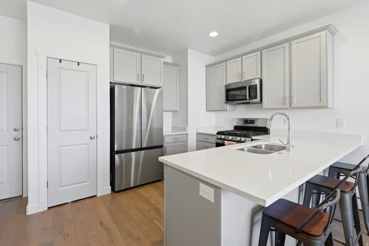 Kitchen featuring light gray cabinetry, stainless steel appliances, a double basin sink with a high-arc faucet, and wood-finish flooring