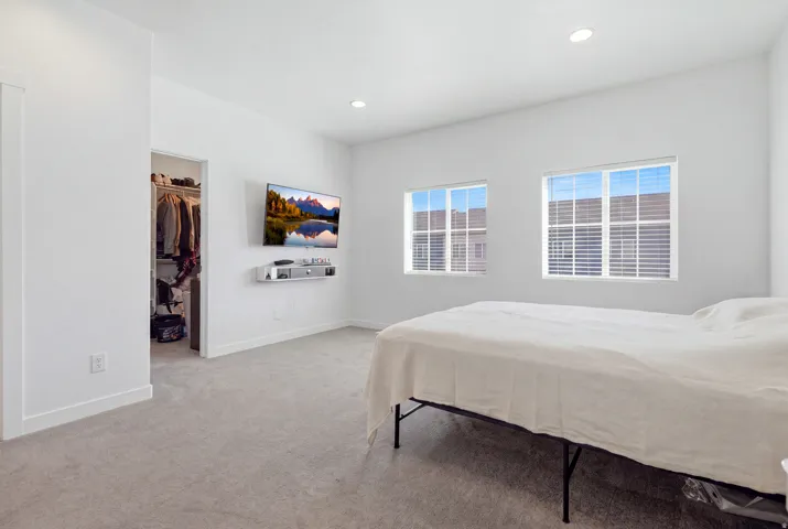 Recessed lighting, light gray carpet flooring, two windows with blinds, and a built-in closet with shelving