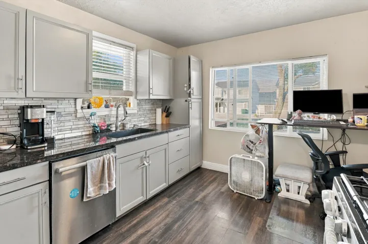 Kitchen featuring light gray cabinetry, dark countertops, a tile backsplash, and wood-finish flooring
