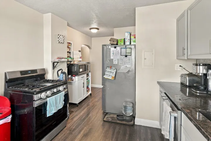 Kitchen featuring wood-finish flooring, dark stone countertops, light gray upper cabinetry, and a stainless steel range