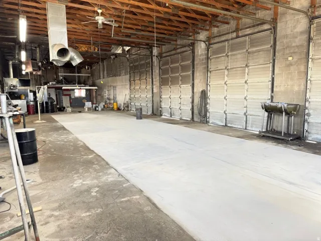 Industrial space featuring multiple roll-up doors, exposed wood beam ceiling, concrete block walls, and overhead lighting