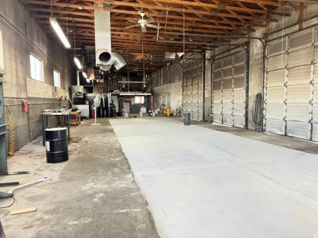 High ceilings with exposed wood beams, multiple industrial roll-up doors, concrete flooring, and ample overhead lighting