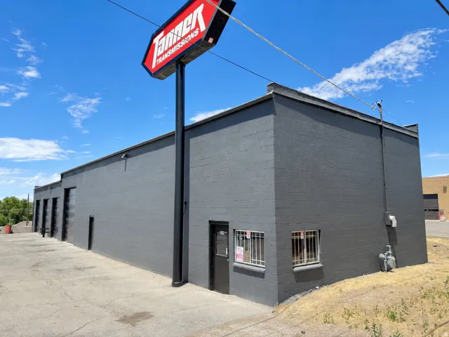 Commercial building with dark gray exterior, multiple roll-up garage doors, a prominent pylon sign, and an entry door with security bars