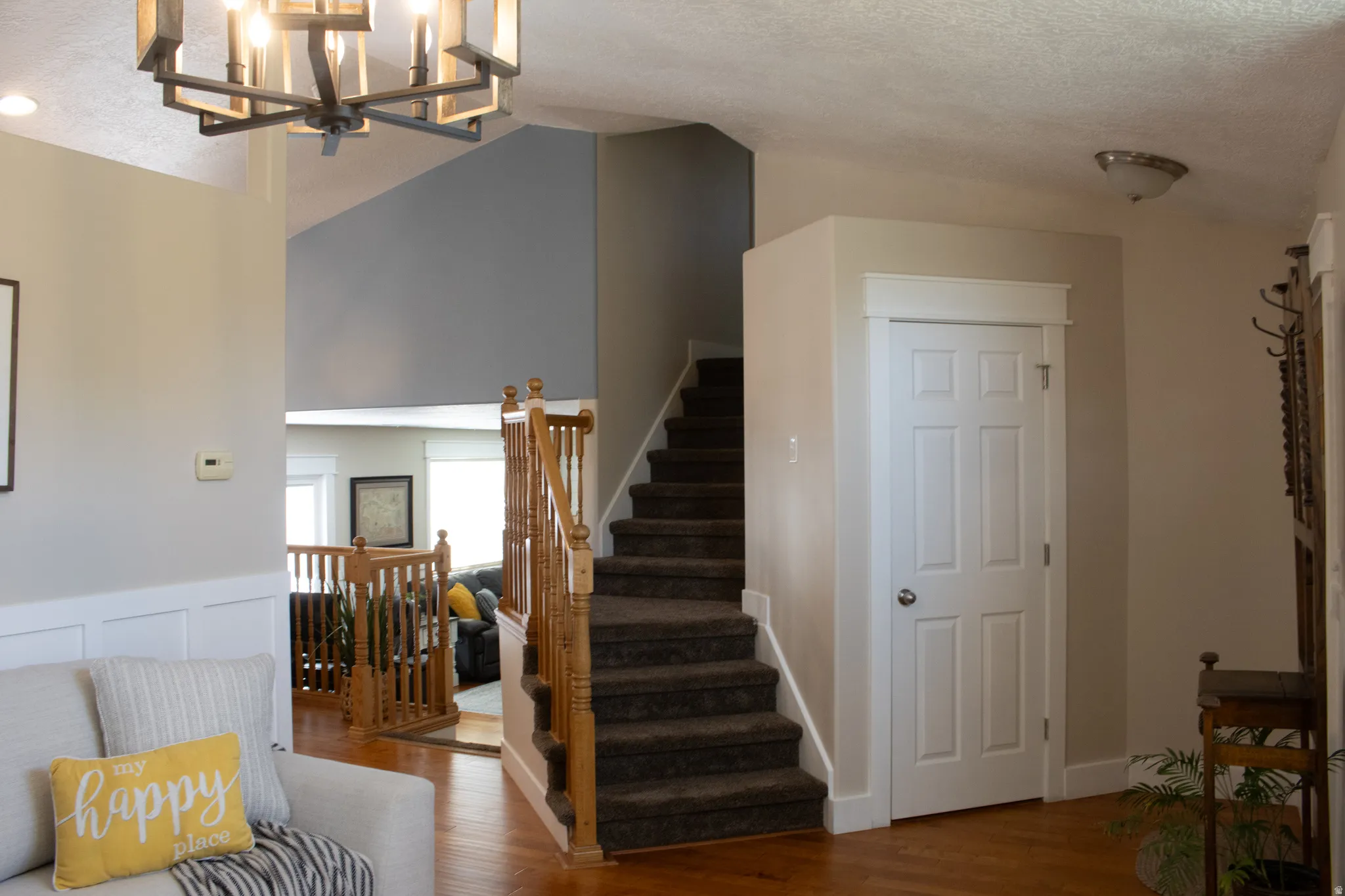 Vaulted ceiling, open wood spindle railing, hardwood flooring, paneled interior door, and modern chandelier