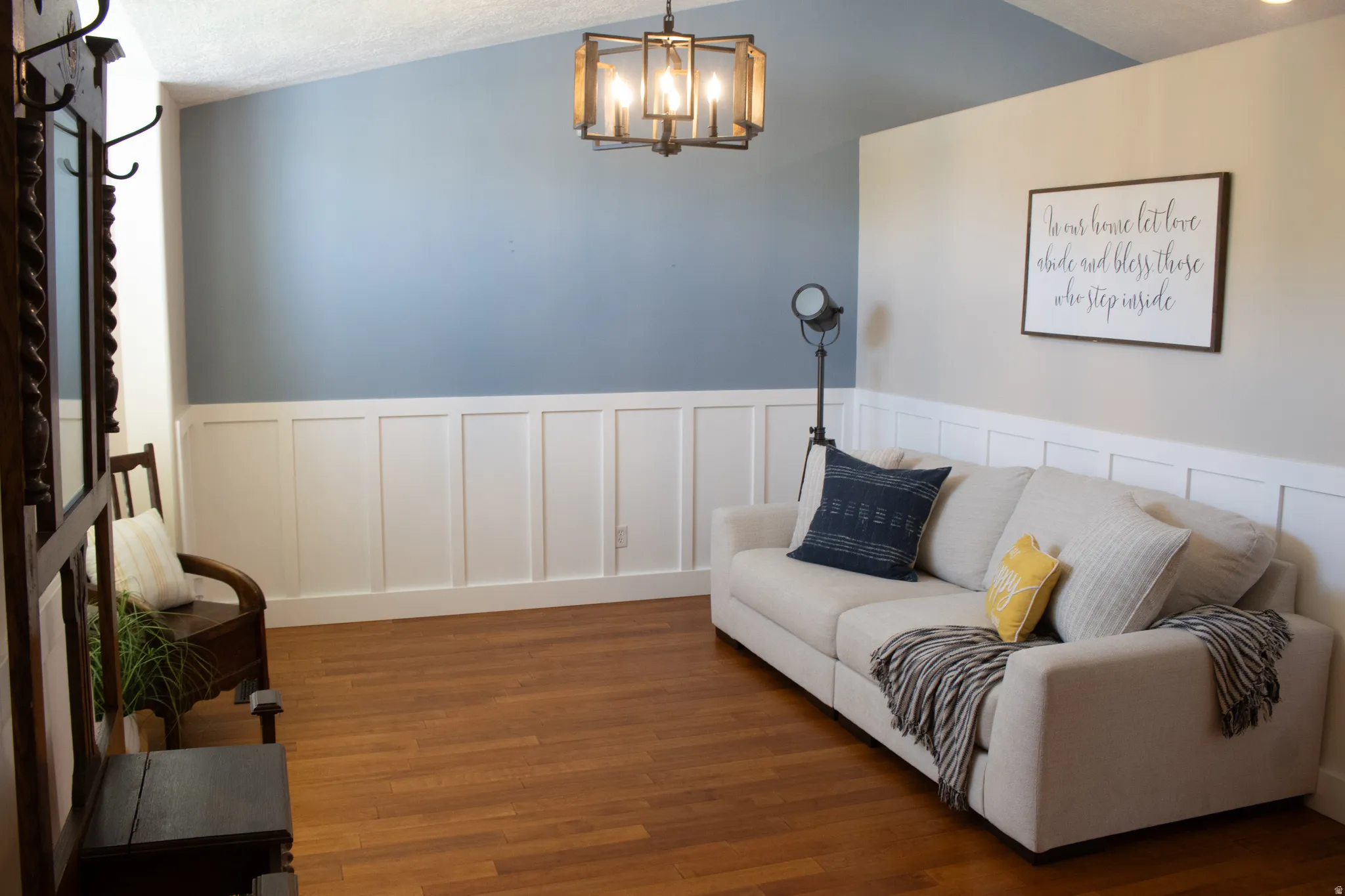 Vaulted ceiling with a contemporary chandelier, hardwood-finish flooring, and wainscoting