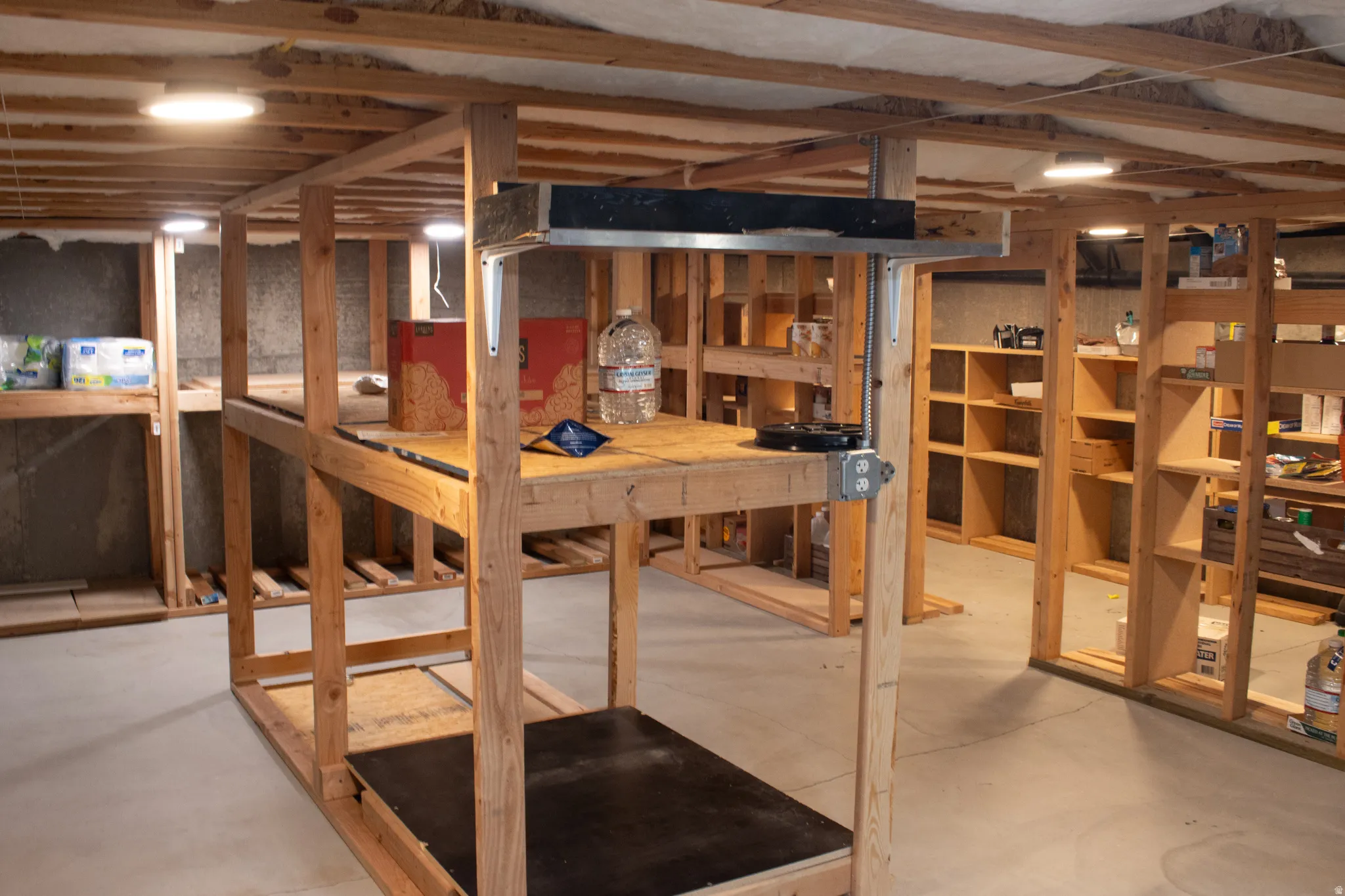 Unfinished basement with exposed ceiling joists and concrete flooring, featuring multiple built-in shelving units and recessed lighting fixtures