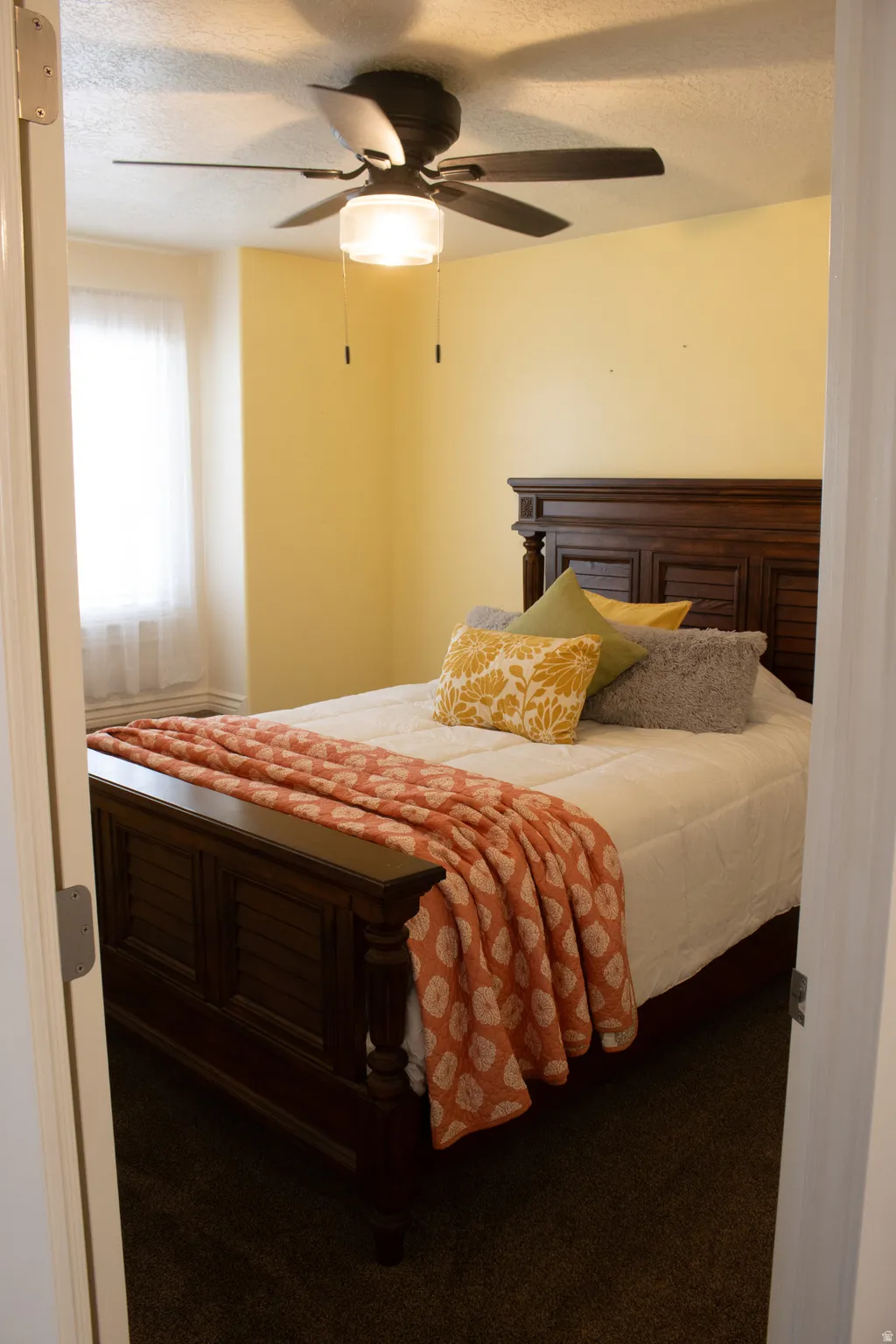 Recessed window with sheer privacy covering, ceiling fan with integrated lighting, and dark tone carpet flooring