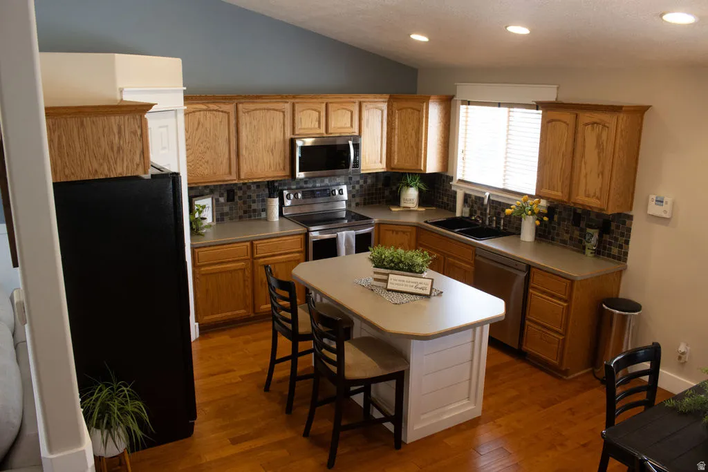Kitchen featuring wood-finish cabinetry, stainless steel appliances, a tiled backsplash, and a central island with seating