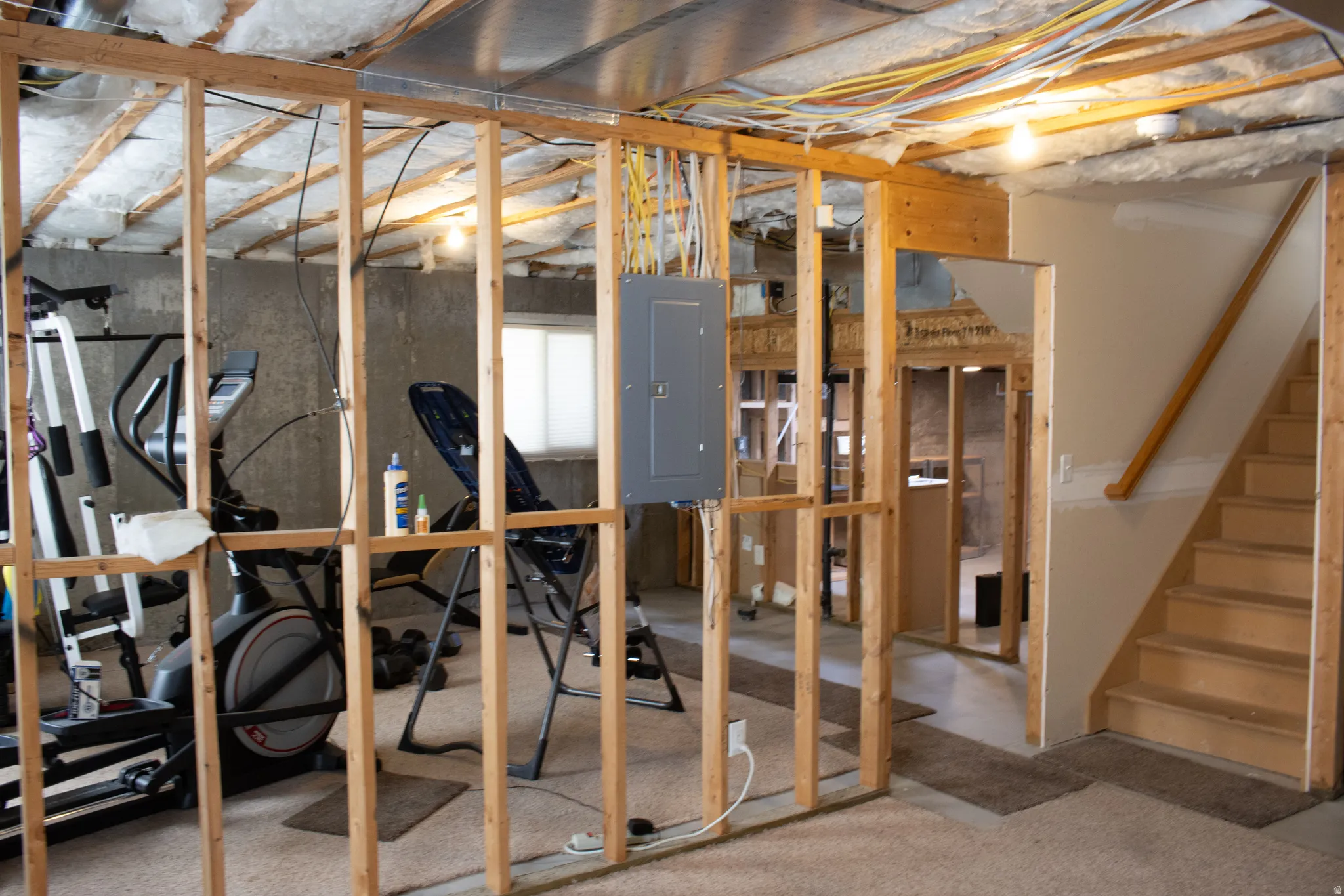 Unfinished basement space featuring exposed wood framing, concrete walls, and visible insulation