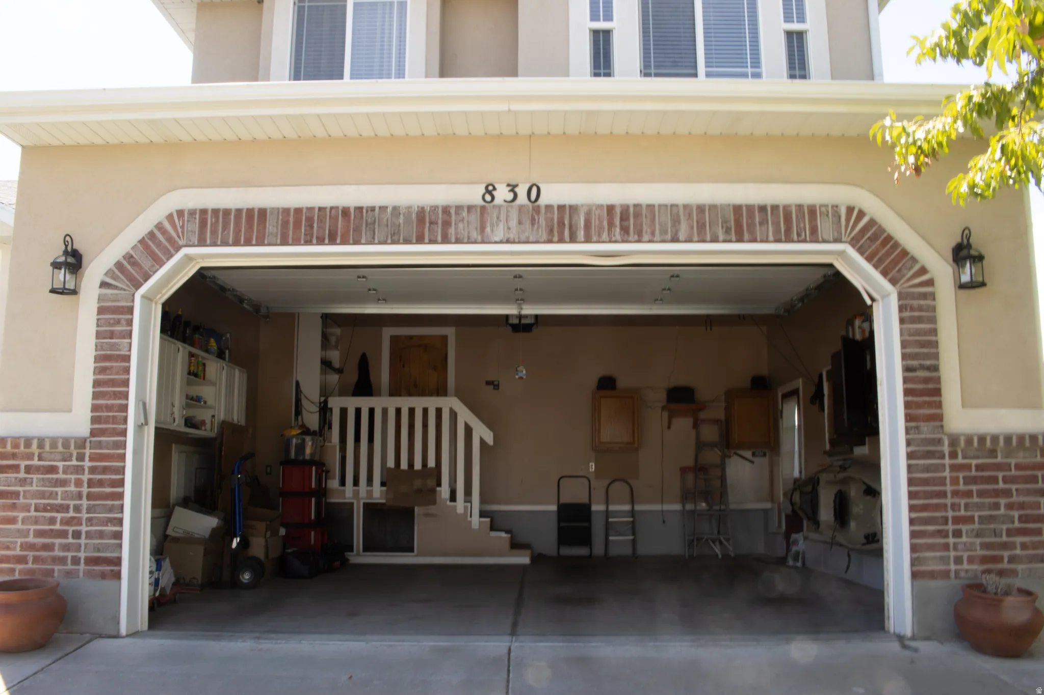 Multi-car garage with brick and stucco exterior, integrated address numerals, and twin exterior wall lanterns