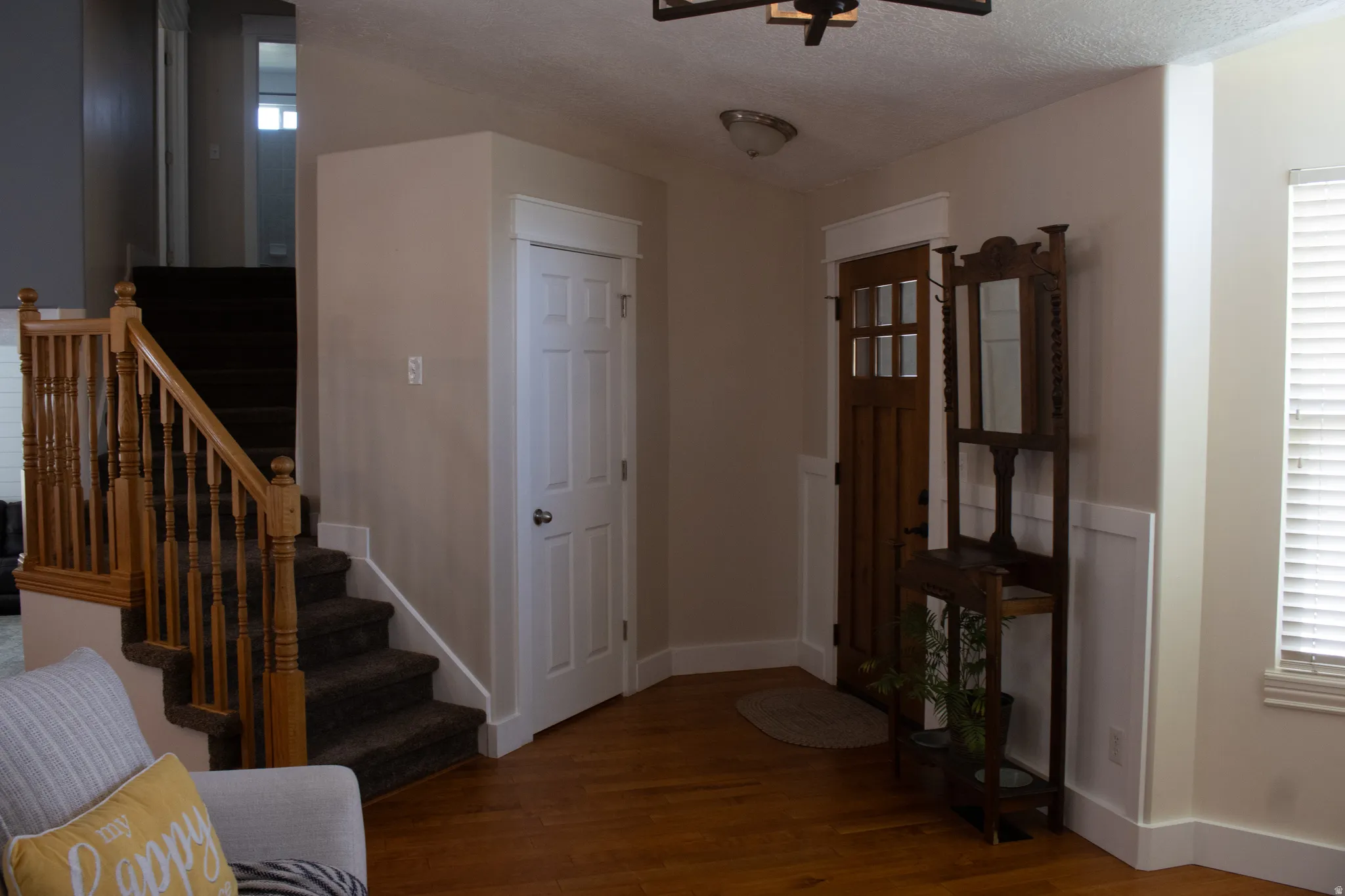 Hardwood flooring with a natural finish, solid panel interior door, wood staircase with balusters, and wainscoting