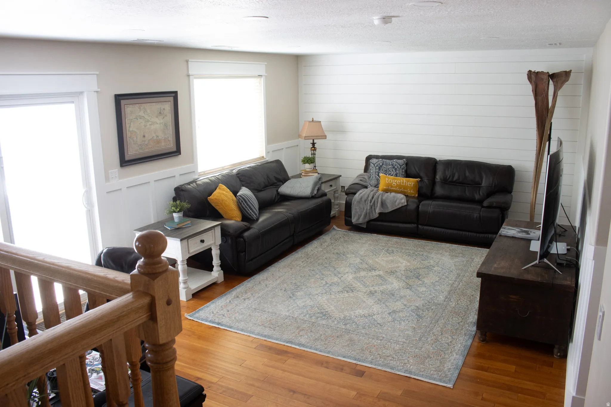 Hardwood-finish flooring, white shiplap accent wall, white wainscoting, sliding glass door, and natural wood railing