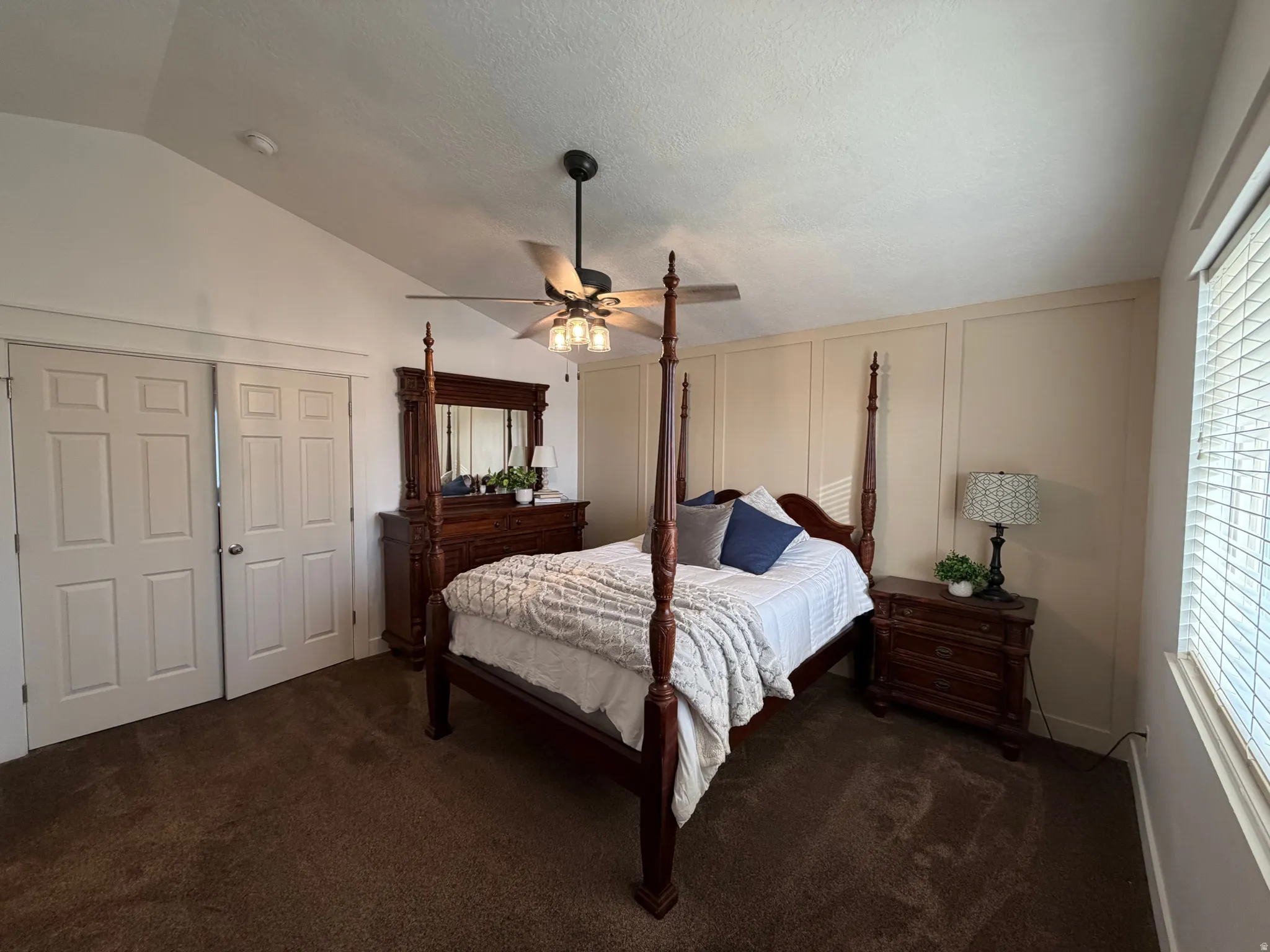 Vaulted ceiling with a ceiling fan light fixture, vertical panel accent wall, and window with horizontal blinds