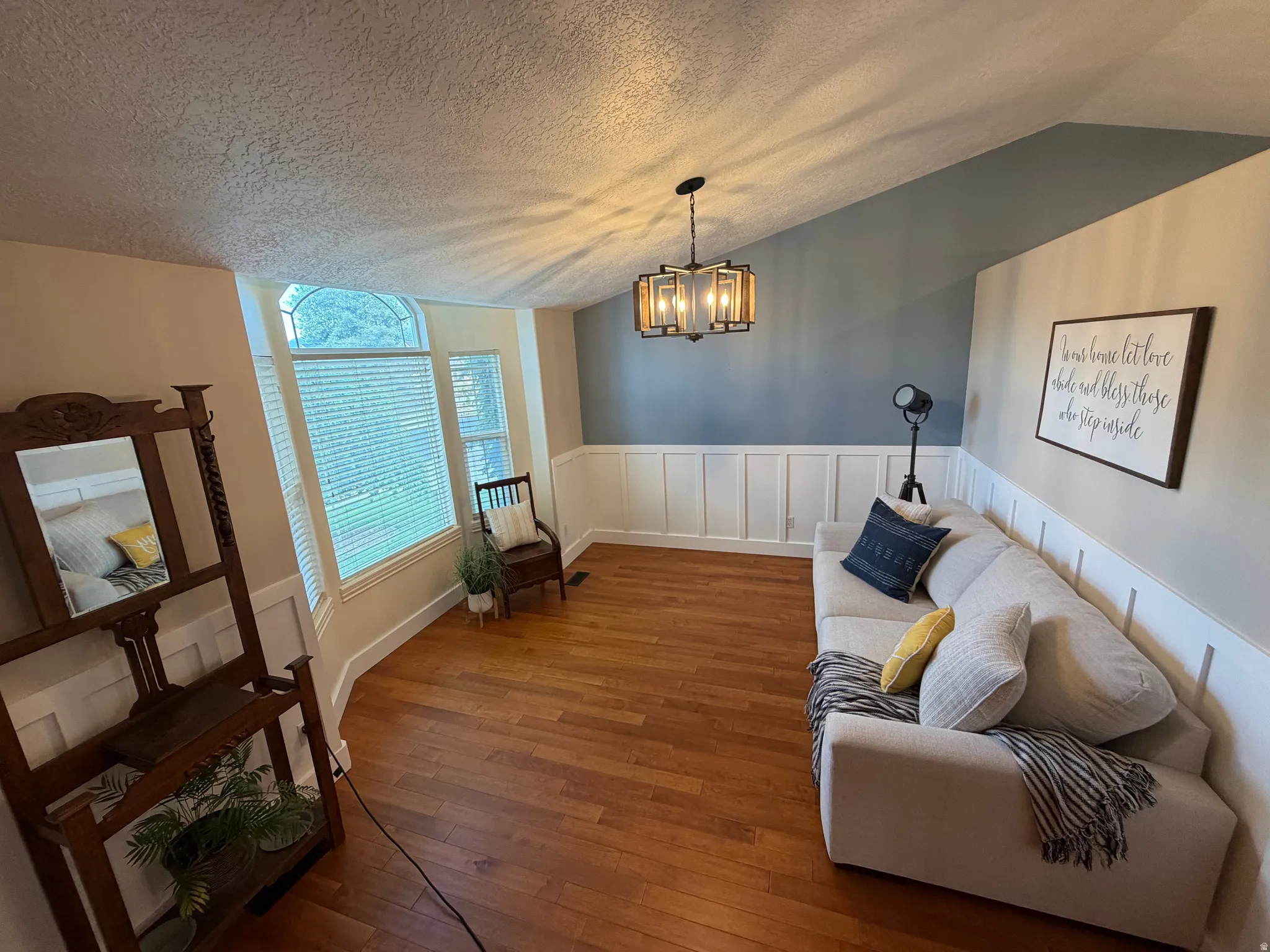 Vaulted ceiling, wood-finish flooring, wainscoting, arched window, and a decorative chandelier